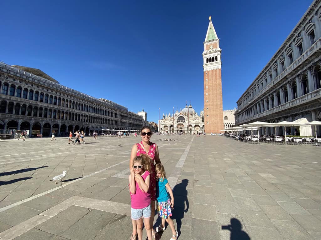 Jude, Martha and Chloe standing in St Mark's square, Venice. St Mark's cathedral and it's bell tower are in the background.