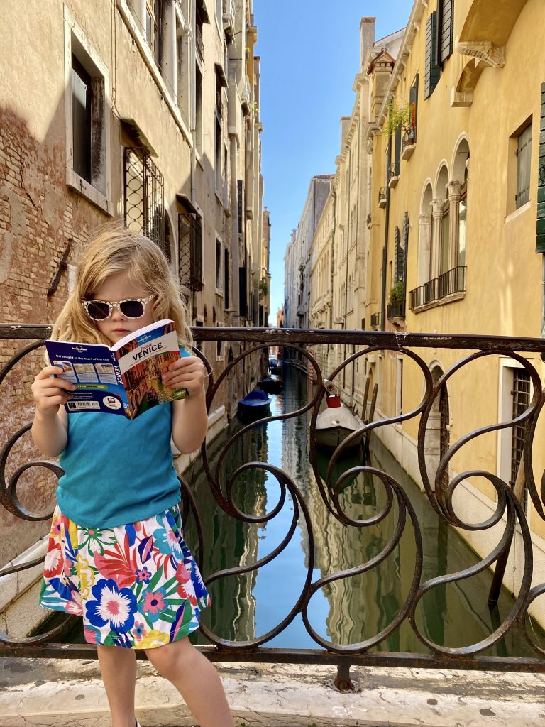 Child reading guide book on bridge in Venice