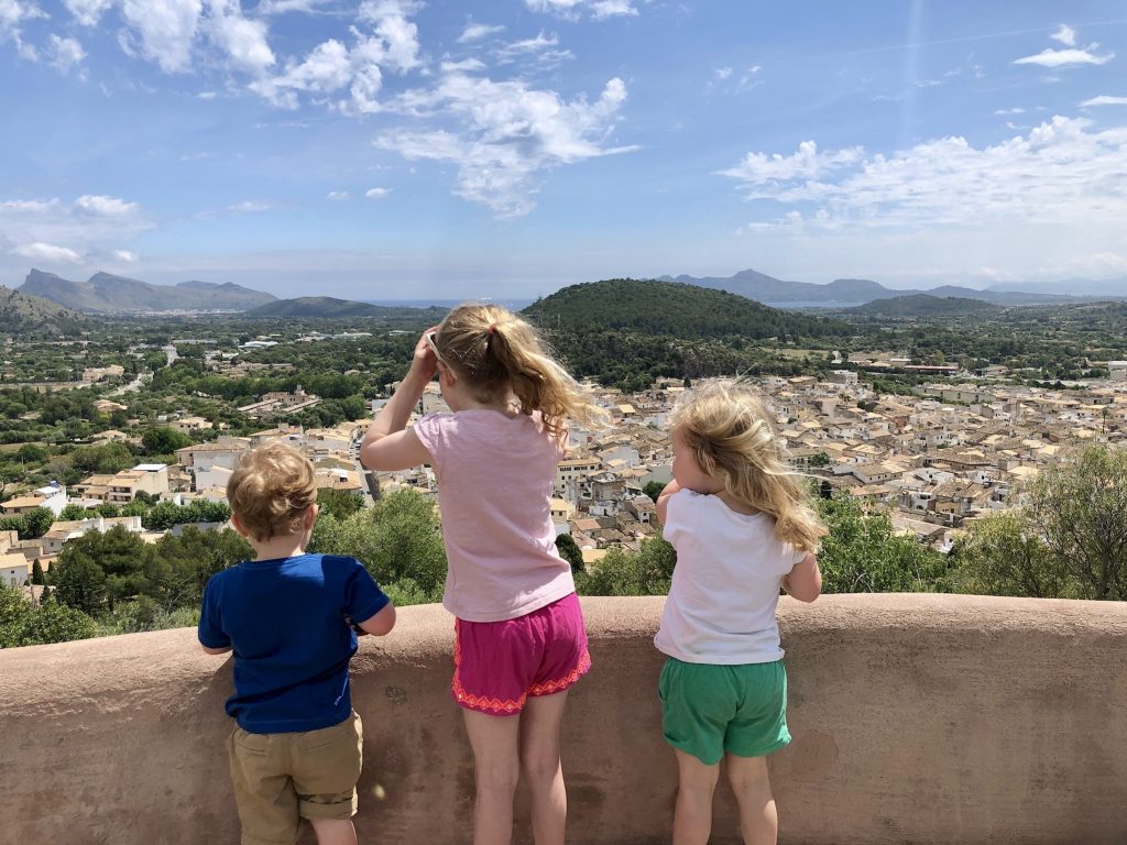 Three children looking out at a view of Pollença old town from the top of the Calvari steps