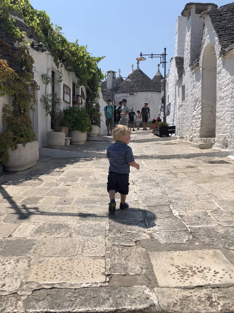 A toddler wandering past the conical trulli houses in Alberobello, Italy,