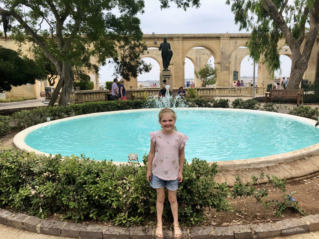 Chloe standing in front of an azure fountain in the upper Barrakka gardens of Valletta, Malta.
