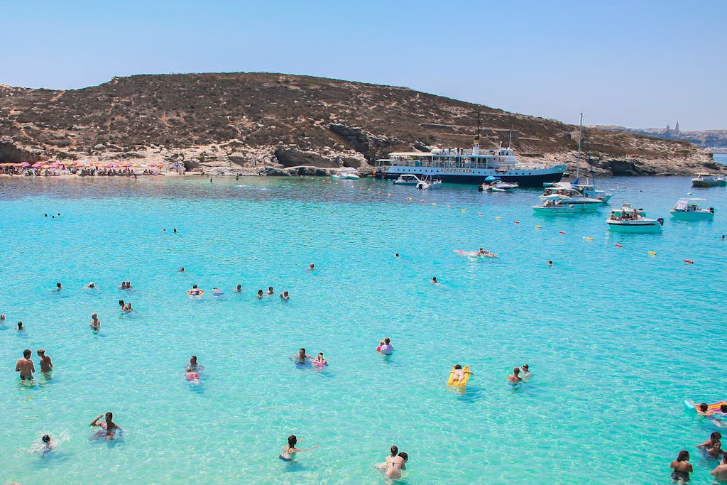 Idyllic scene of swimmers and boats at Malta's Blue Lagoon on a sunny summer day.