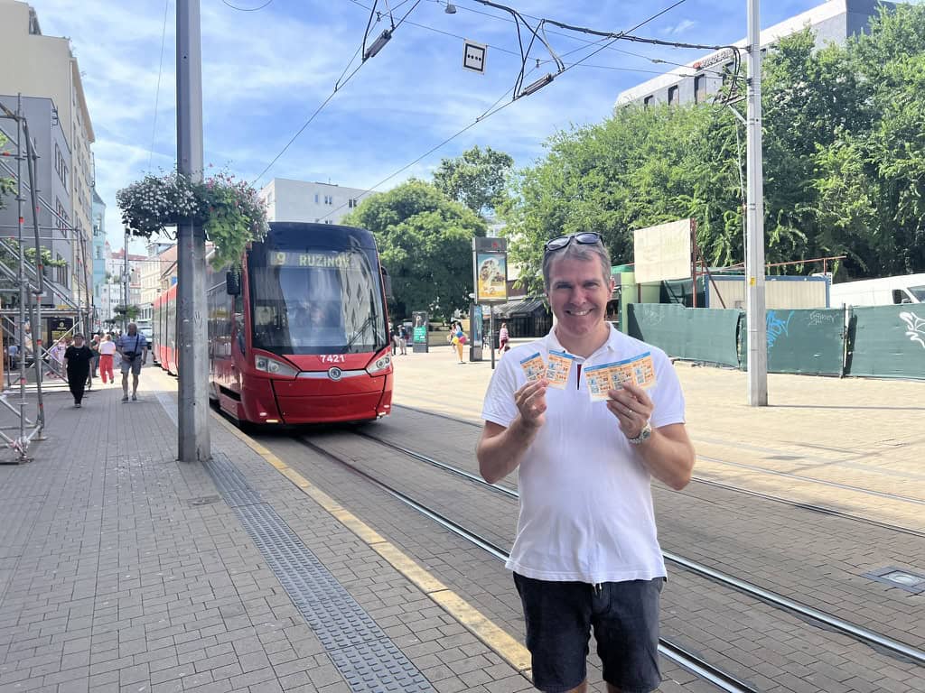 Adam displaying the tickets for the Bratislava tram, bought from the local Tabak, with a tram arriving in the background. 