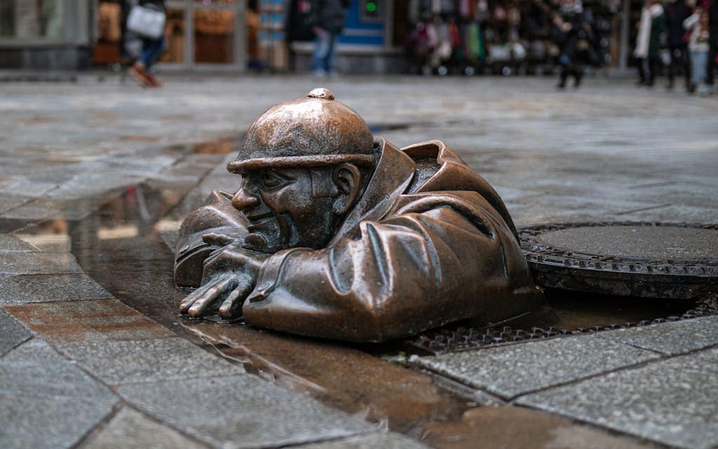 A unique bronze statue emerging from a manhole on a bustling city street in Bratislava.