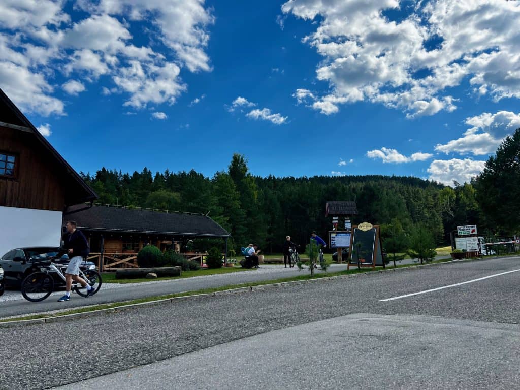 The road and buildings in the small village of Podlesok, with forest covered hills visible in the background.