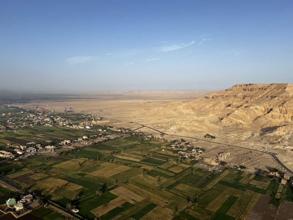 Views from a luxor hot air balloon of green fields meeting the dry brown desert, fringed by mountains. 