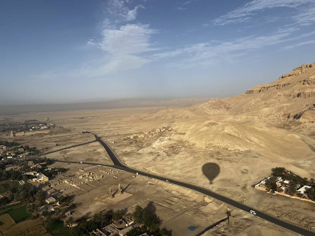 View from the hot air balloon in Luxor of the desert, with the Collosi of Memnon visible and the hot air balloon shadow.