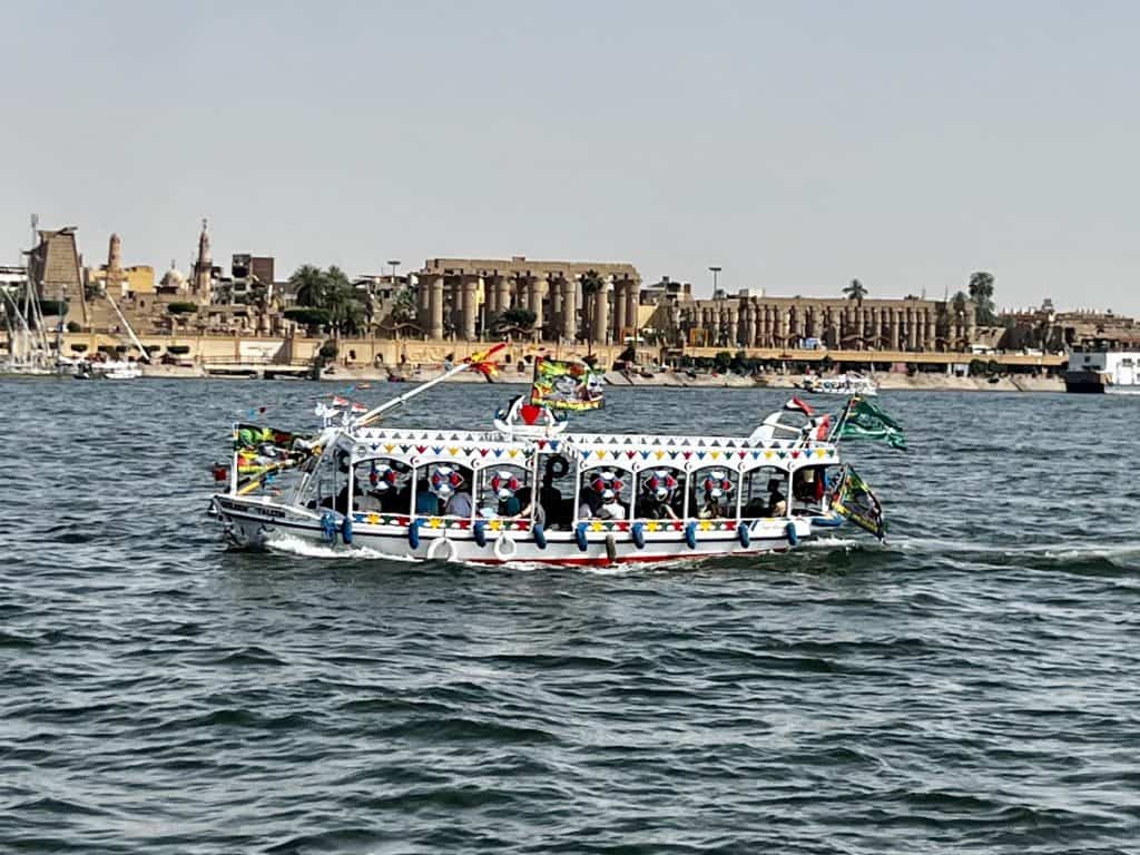 One of the many taxi boats that can be used to cross the river Nile with Luxor temple in the background. 