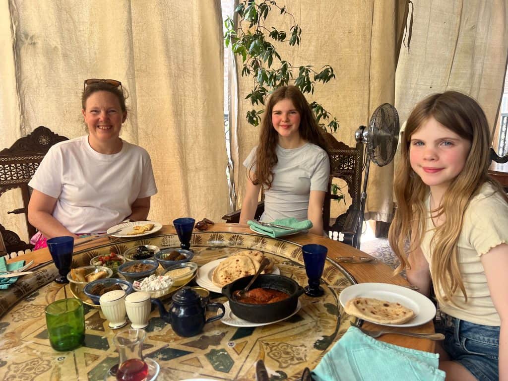 Our family eating Mezze at the Sofra restaurant in Luxor. Jude, Chloe and Martha are sitting around a decorative table, with a plant and curtains to keep out the sun in the background. In our opinion this is one of the best restaurants in Luxor for families.