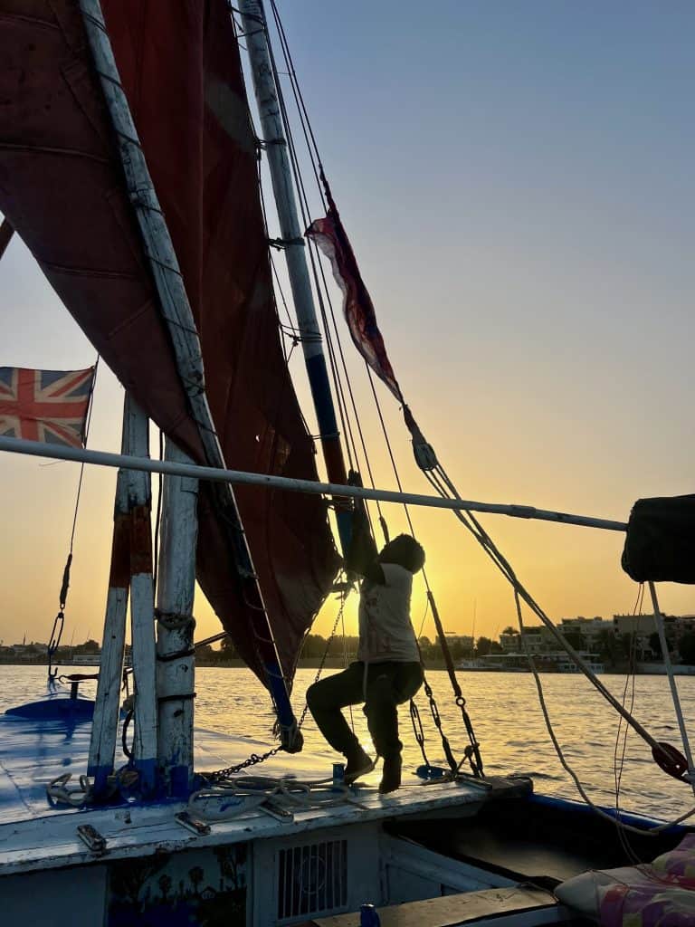 A child hoists the felucca sail in Luxor, Egypt. The sun is setting behind him.