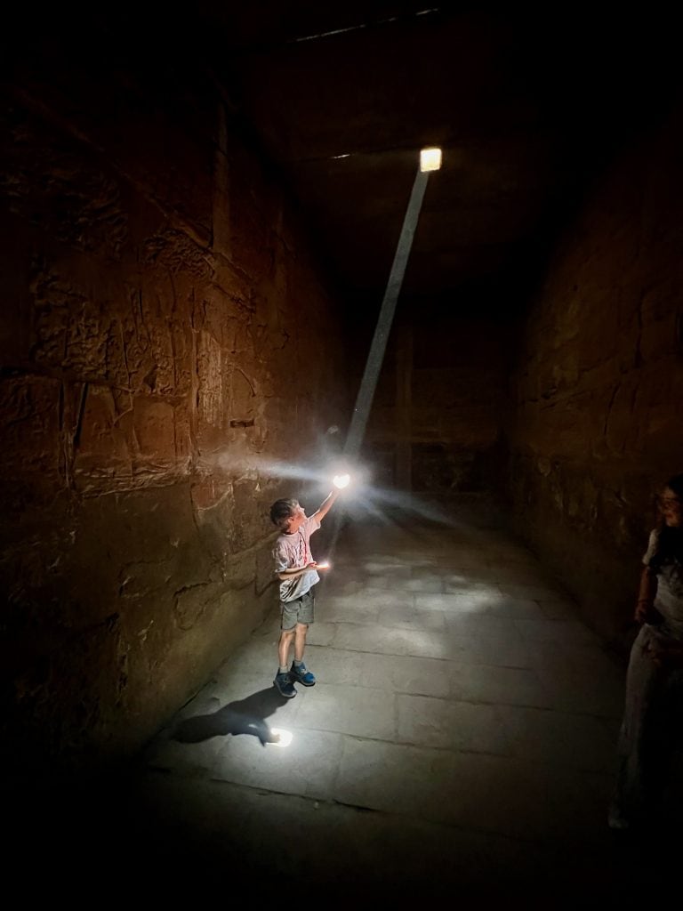 A child in a small dark chapel as the temple of Ramases II at Karnak, Luxor. A bream of light is piercing from a missing brick near the ceiling and the child is catching it in his hands. 