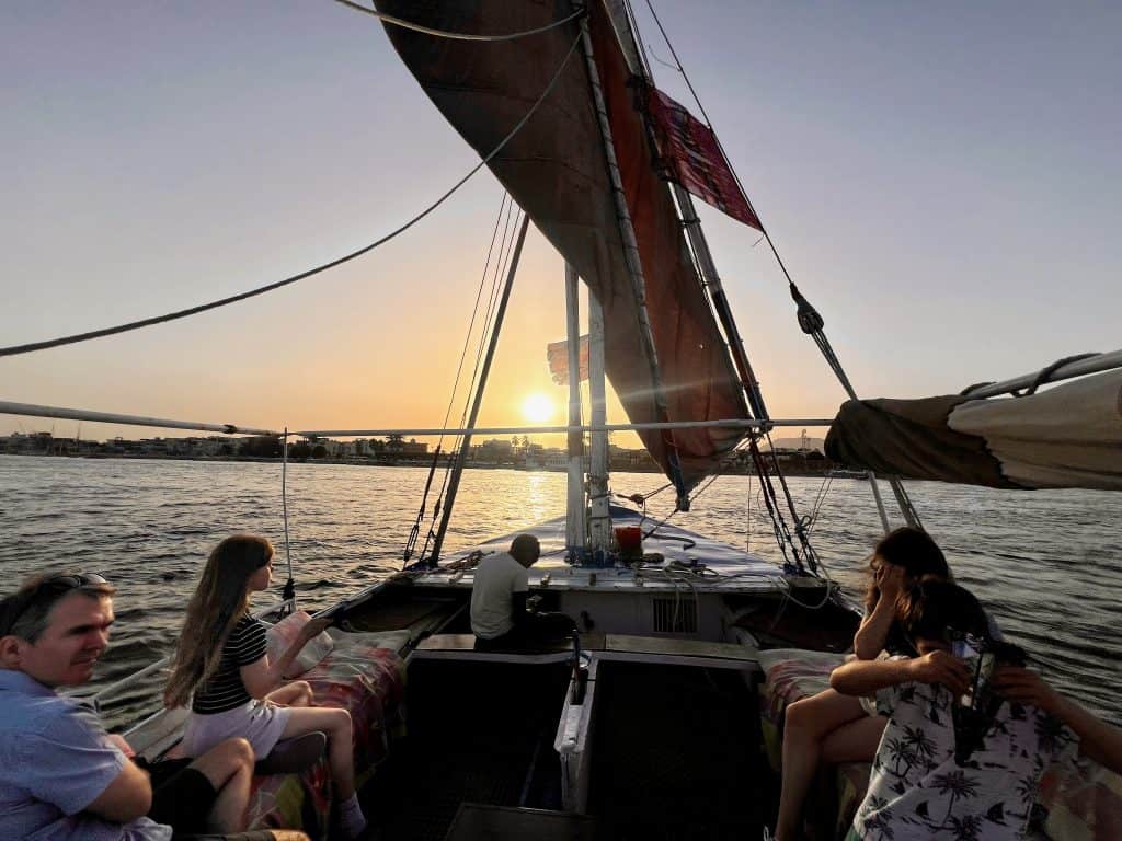 Family on a felucca on the Nile in Luxor, Egypt. In the background the sun can be seen setting beyond the far river bank.