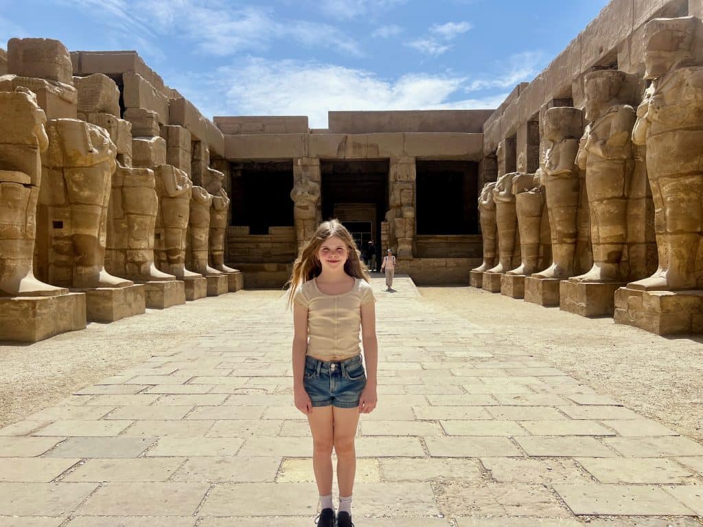 Martha stands in Karnak temple, one of the best things to do inLuxor Egypt. She is in an open area surrounded by large statues