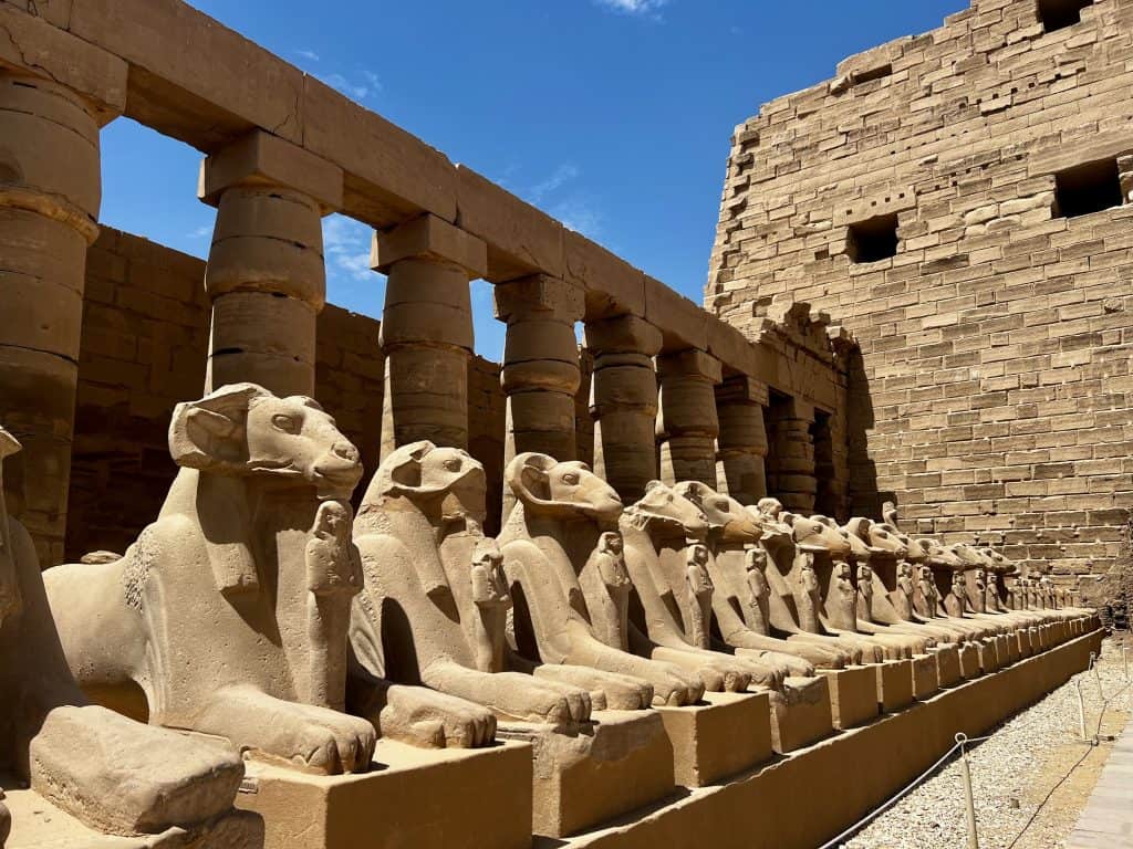 A line of ram statues in front of a columned wall at Karnak Temple in Luxor, Egypt.