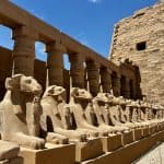 A line of ram statues in front of a columned wall at Karnak Temple in Luxor, Egypt.