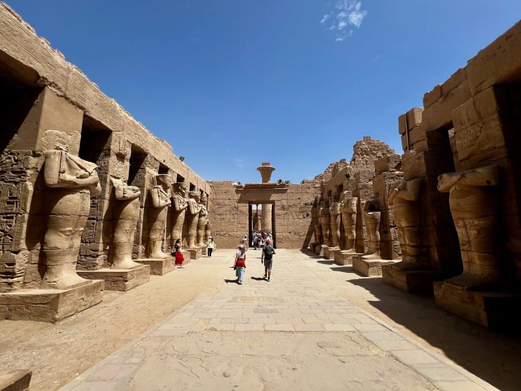 A view of the main hallway of the temple of Ramases III in the Karnak temple complex in Luxor. Egypt. The wide walkway is lined by statues standing in front of pillars, many of which are headless.