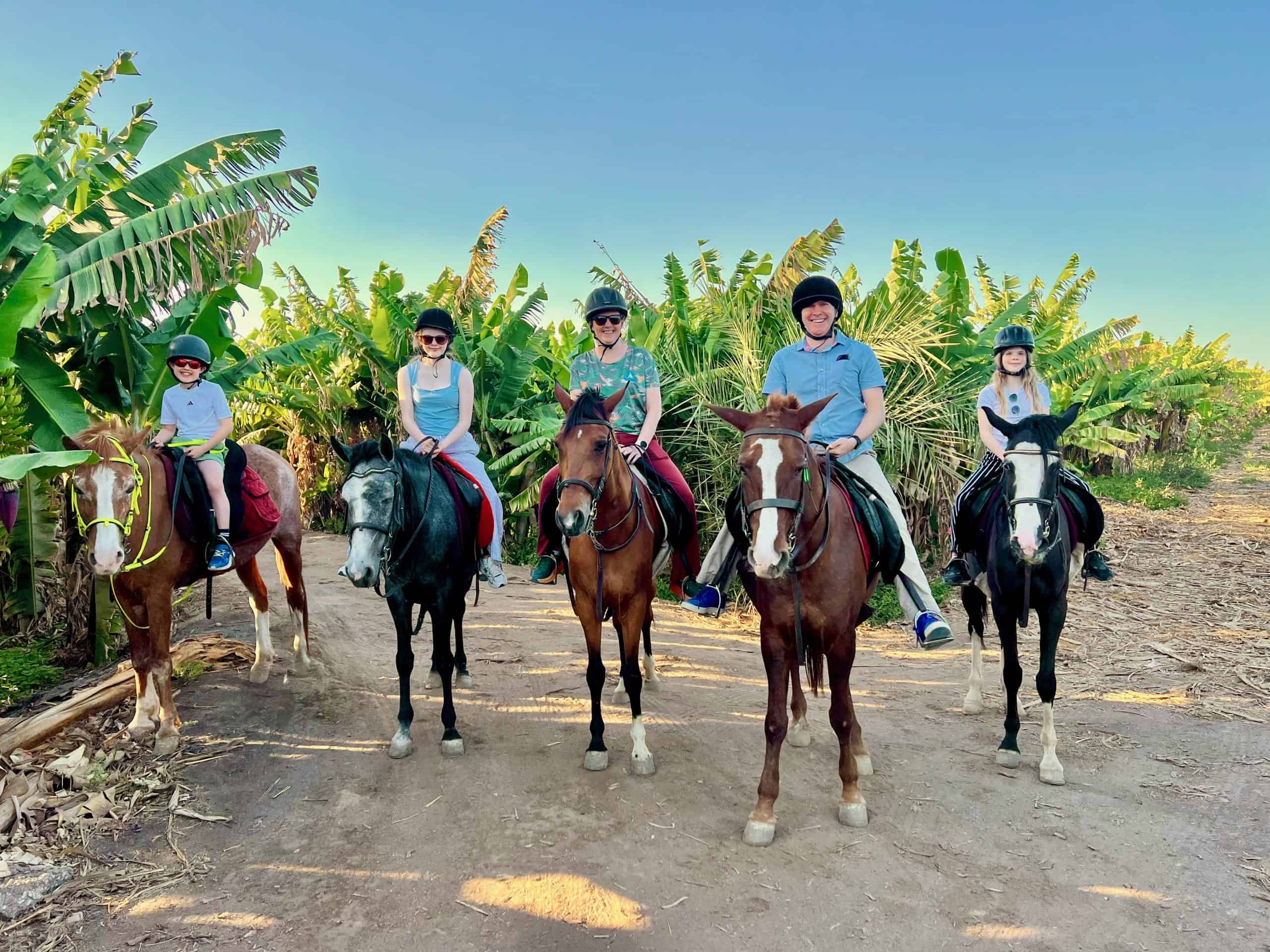 Family on horse back on a dirt track through a banana plantation in Luxor, Egypt.
