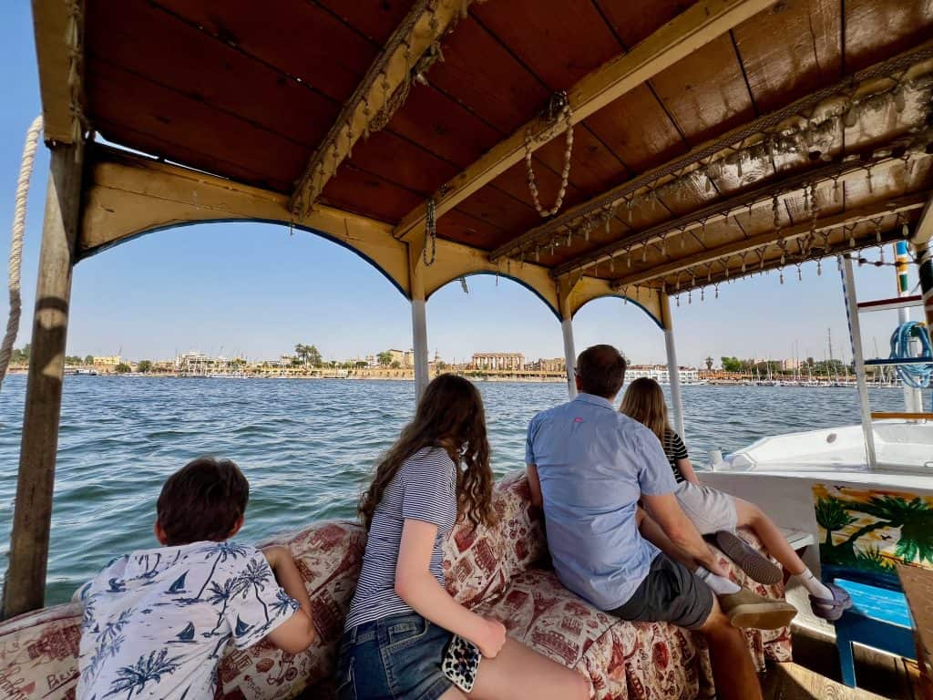 Family sitting on a private taxi boat on the Nile in Luxor, looking out over the river. Luxor temple can be seen in the background on the far bank.