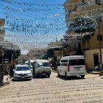 A street view in Luxor, showing cars and minivans driving down the road with buildings on either side.