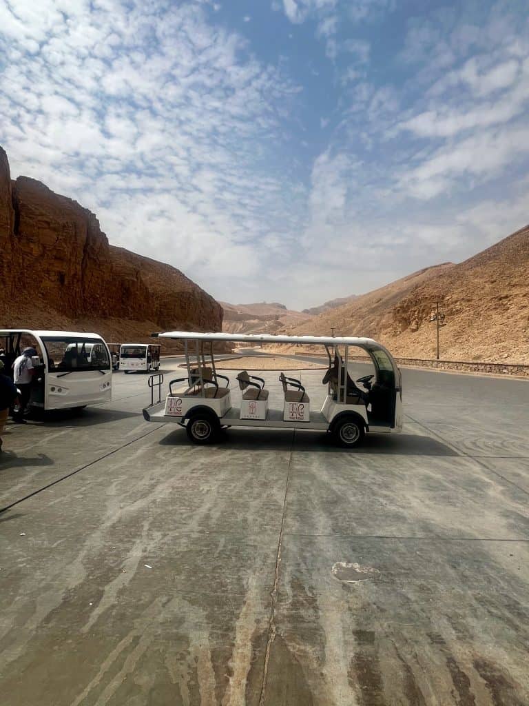 Electric tram parked on the tarmac at the entrance to Valley of the Kings. In the background the road can be seen winding up the valley towards the main site.