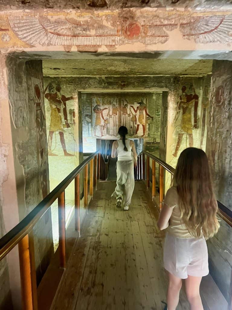 Children walking down the corridor in the tomb of Tausert/ Setnakht in Valley of the Kings, Luxor. On the walls to the side of the wooden walkway can be seen colourful ancient Egyptian images.