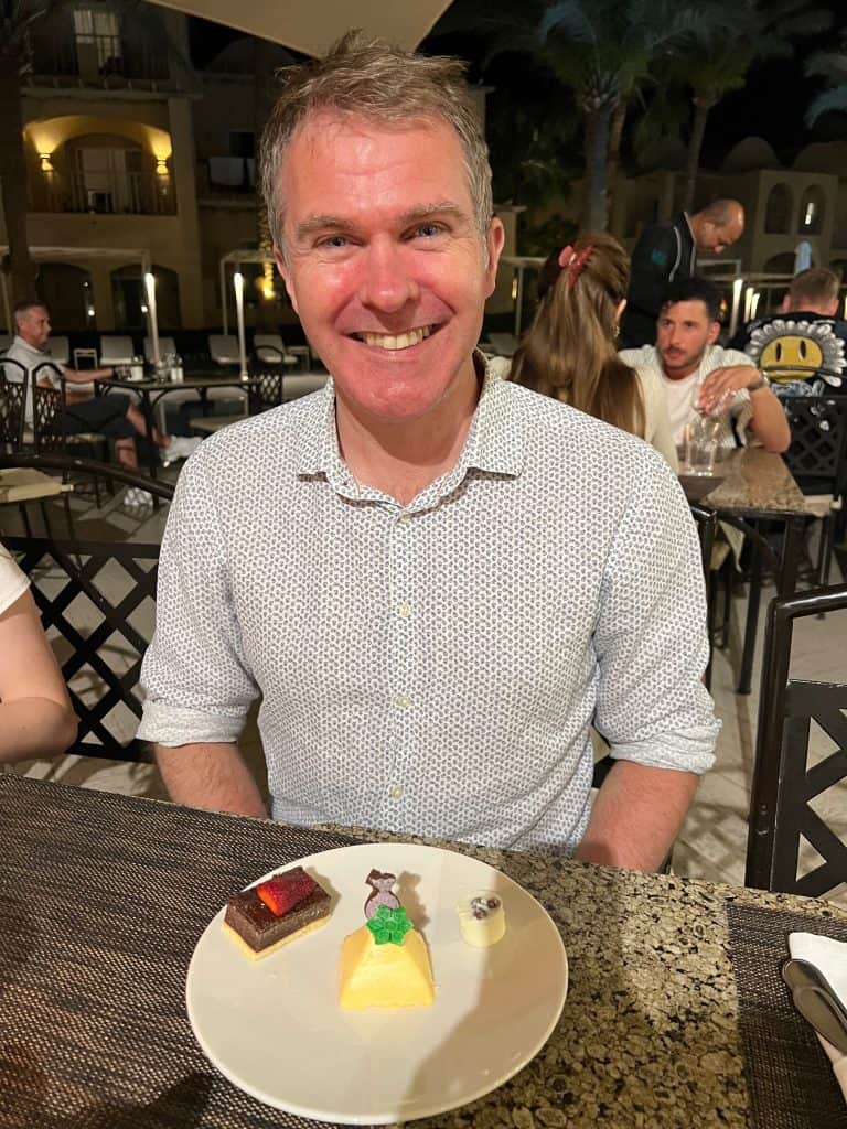 Man sits at a table in the hotel Jaz Makadina restaurant. In front of him is a plate containing three small cakes,