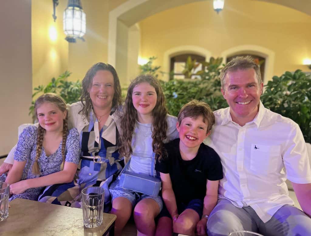 Family of two adults, a teenage girl, 11 year old girl and 9 year old boy sitting together in the bar area of Jaz Makadina hotel.