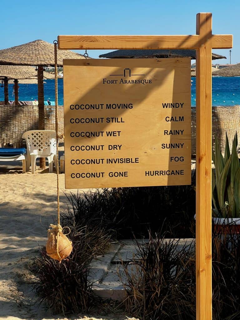 Wooden sign next to the beach at Fort Arabesque hotel in Makadi bay. A coconuts swings off one end of the sign and the sign described what the wheather is depending on what the coconut is doing.