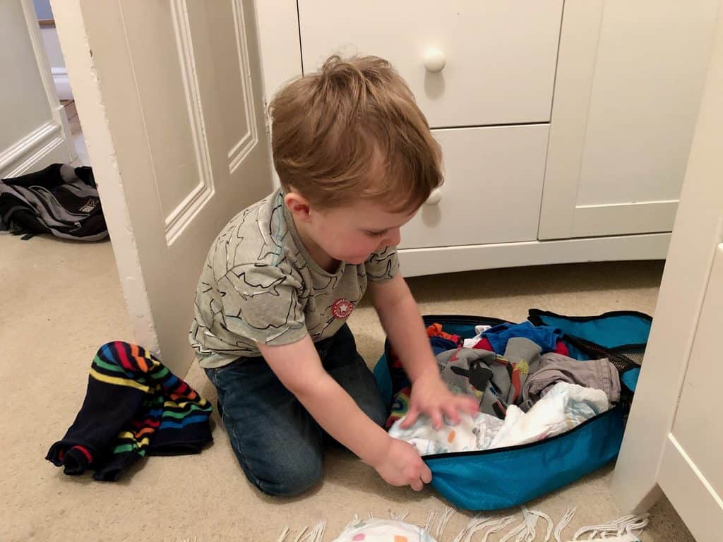 A child packing his clothes into a packing cube ready to go on holiday.