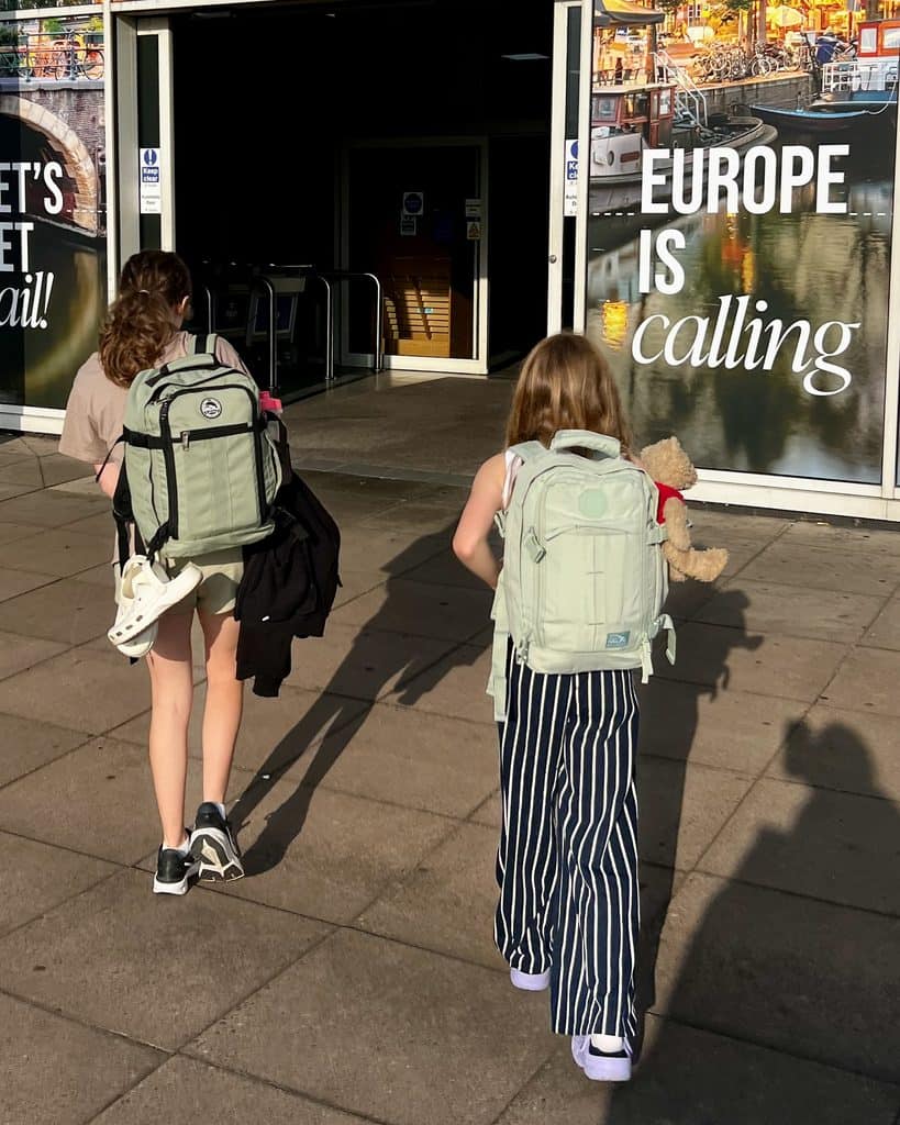 Two girls carry their backpacks towards an open door at a ferry terminal. To the side can be seen the slogan 'Europe is calling'.